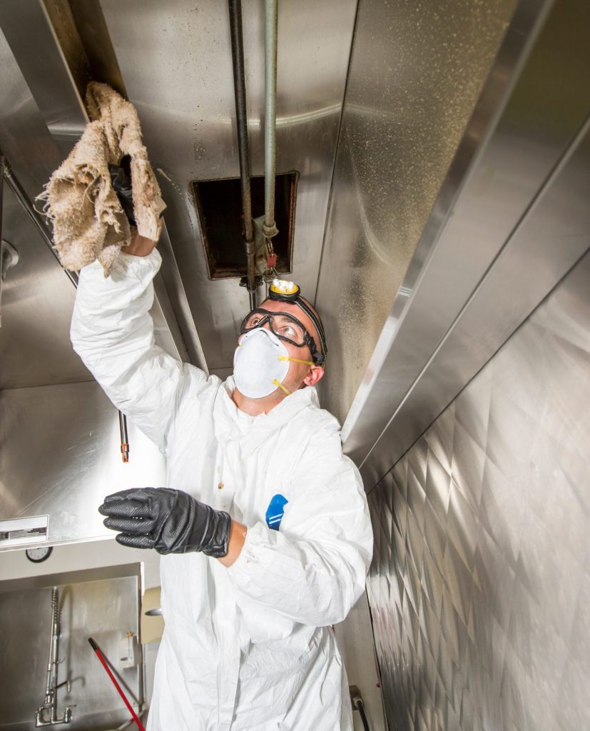 A health inspector examines a commercial kitchen exhaust hood while conducting a restaurant safety inspection.