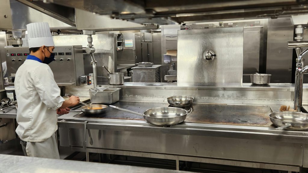 A chef prepares food in a clean commercial kitchen equipped with stainless steel appliances and professional cooking equipment.